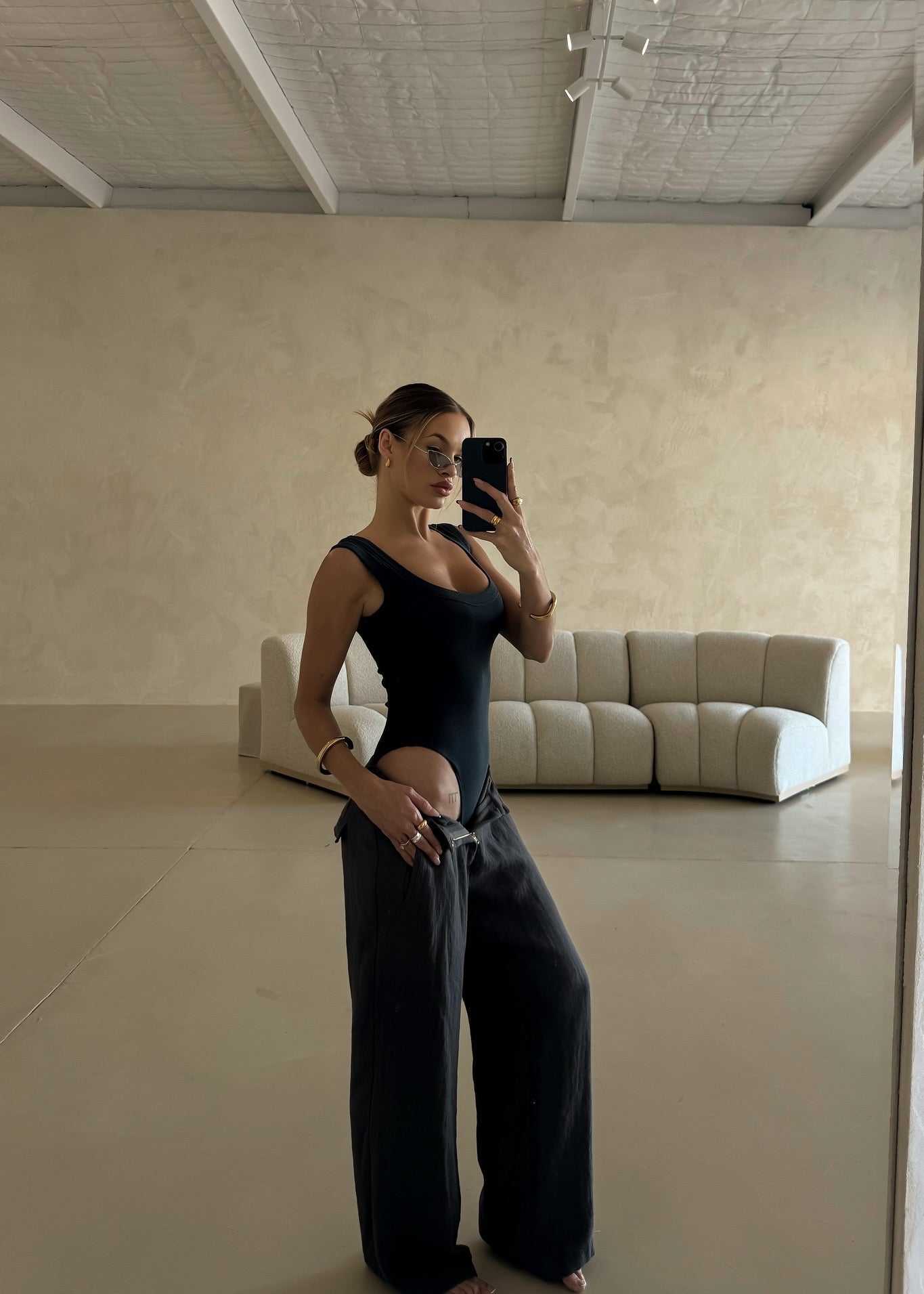 Arian Linen Pant Person taking a mirror selfie in a minimalistic room with a white sofa.