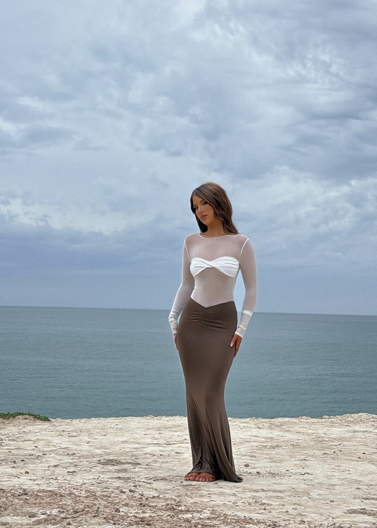 Woman in a two-tone dress standing on a coastal cliff with ocean and sky in the background