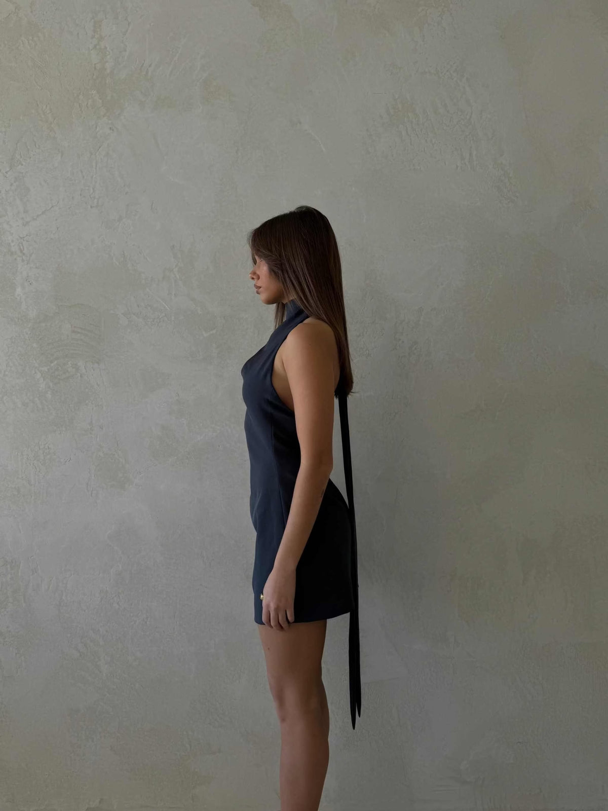 Side view of a woman wearing a deep ocean blue Xara Mini Halter Dress with a high halter neck and low back design, showcasing the dress's structured fit and snatched waist.