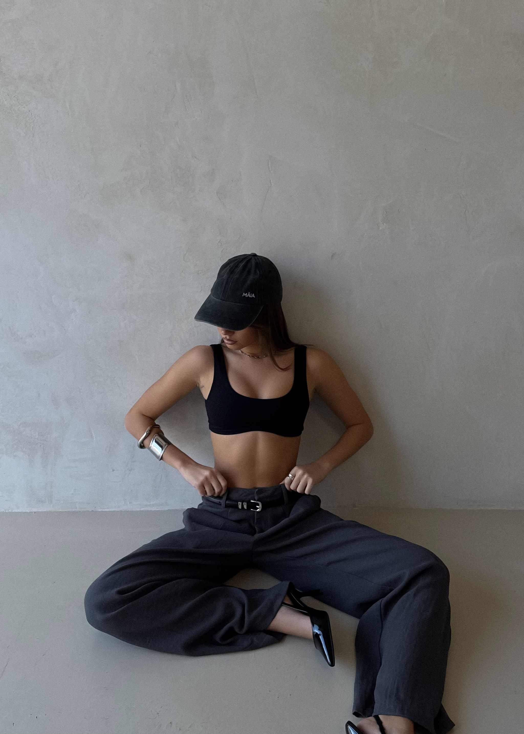 Arian Linen Pant Person wearing a black cap, sports bra, and wide-leg pants sitting on a light-colored floor against a plain wall.