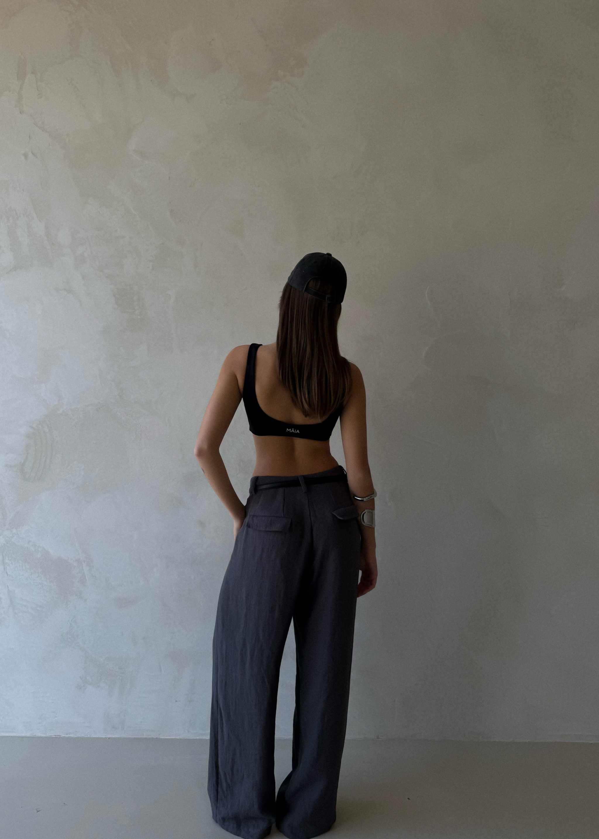 Arian Linen Pant Person wearing a black sports bra and gray wide-leg pants against a plain wall.